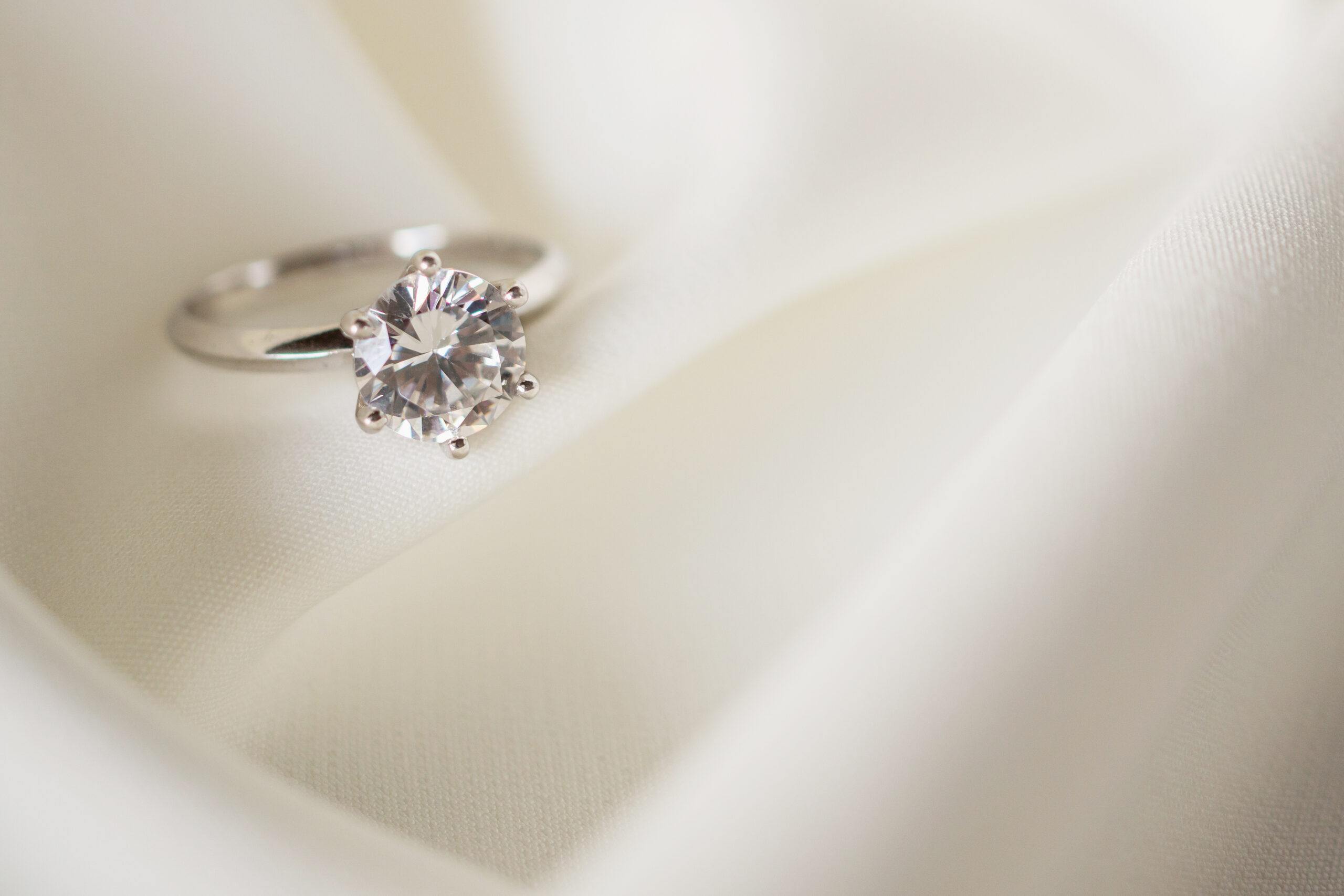 Diamond solitaire ring resting on cream silk